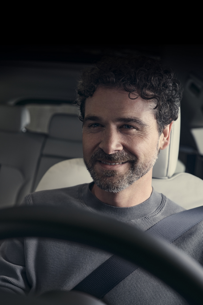 Мъж, който се усмихва, сниман в седалката на водача на изцяло новата Mazda CX-60 SUV.