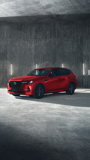 A red Mazda CX-60 Plug-In Hybrid SUV parked in front of a modern building.