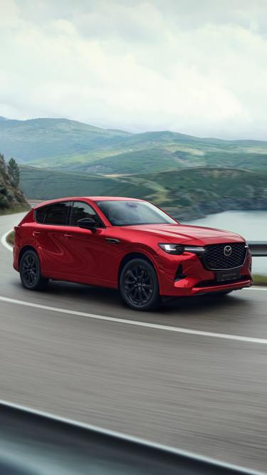 A red Mazda CX-60 Plug-In Hybrid SUV driving around a curve on a coastal highway.