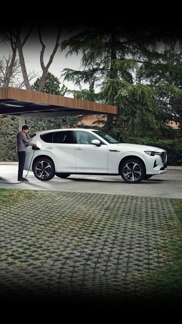 A white Mazda CX-60 Plug-In Hybrid parked in front of a modern home with lots of trees around.