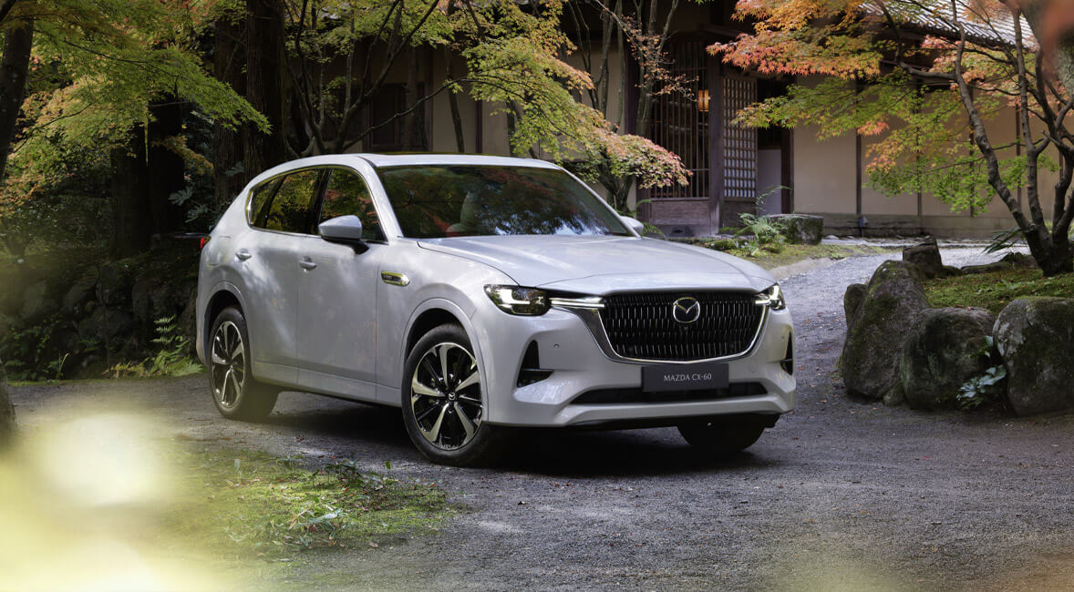 Helt nye Mazda CX-60 ladbar hybrid-SUV vist forfra, parkert ved en slette med trær.