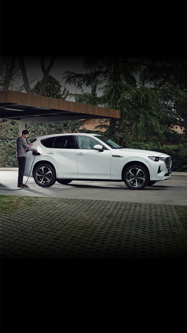 En hvit Mazda CX-60 Plug-In Hybrid SUV parkert foran et moderne hjem omgitt av mange trær.