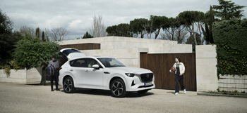 Een geparkeerde witte Mazda CX-60 plug-in hybride SUV, samen met een man en een vrouw die buiten staan en een basketbal vasthouden.