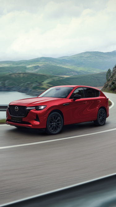 Červená Mazda CX-60, plug-in hybridní SUV, projíždějící zatáčkou na pobřežní dálnici.