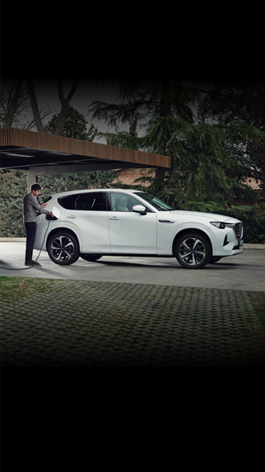 Een witte Mazda CX-60 Plug-in hybride geparkeerd voor een modern huis tussen de bomen.