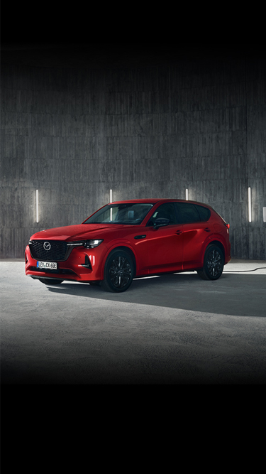 Um SUV híbrido plug-in Mazda CX-60 vermelho estacionado em frente a um edifício moderno.