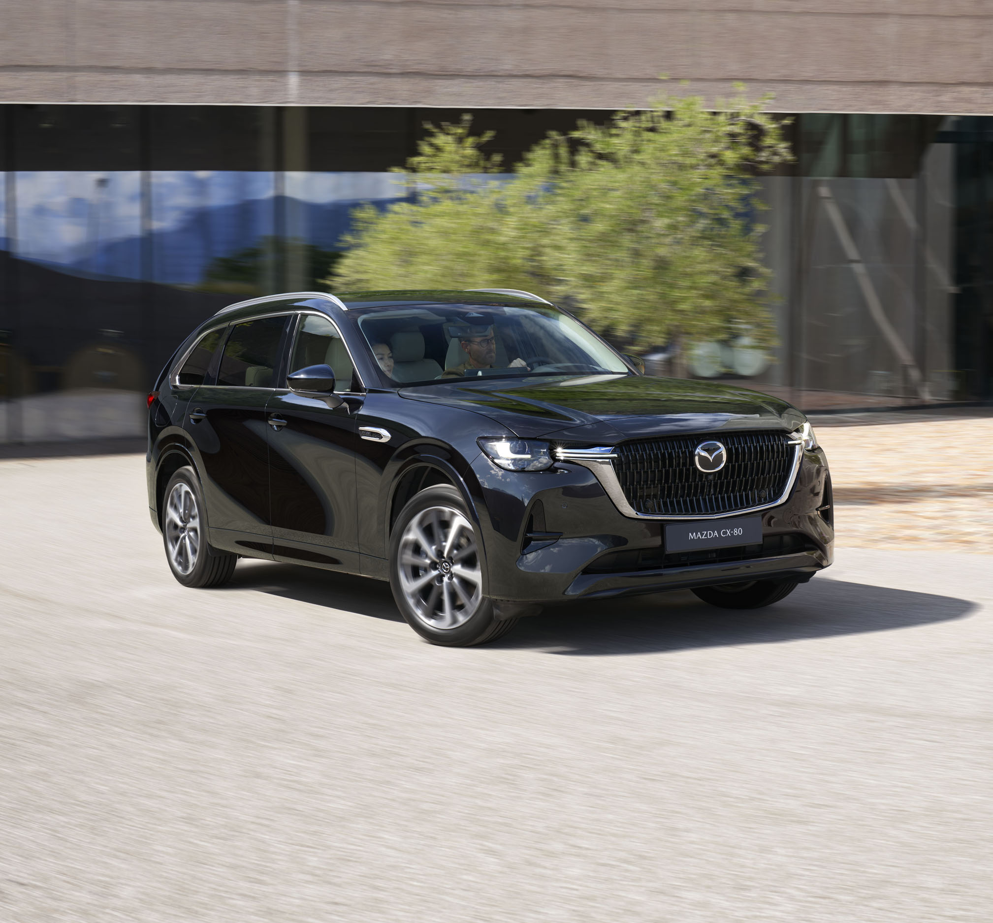 Černá Mazda CX-80 zaparkovaná před budovou.