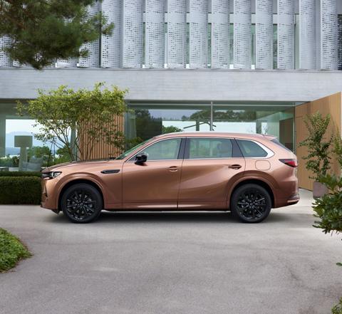 Seitenansicht eines vor einem Haus mit Glaswand geparkten Mazda CX-80.