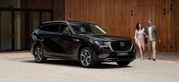 The Mazda CX-80 parked in front of a building and a couple walking around it.