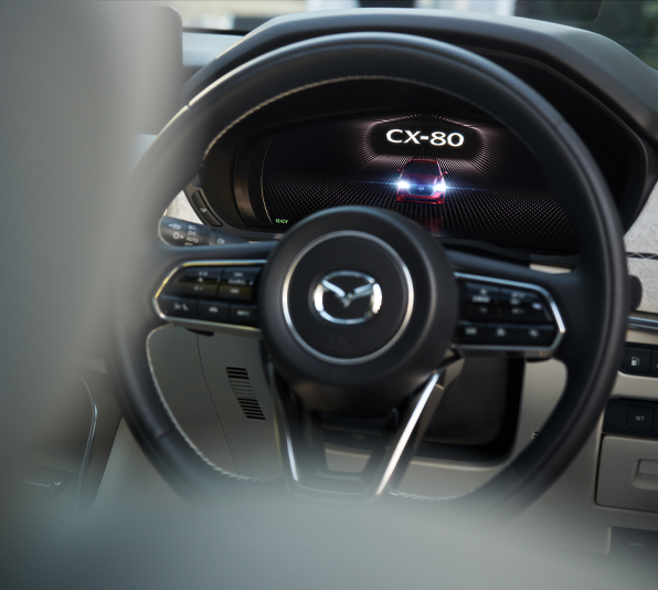 A close-up of the steering wheel of the Mazda CX-80 and its logo.