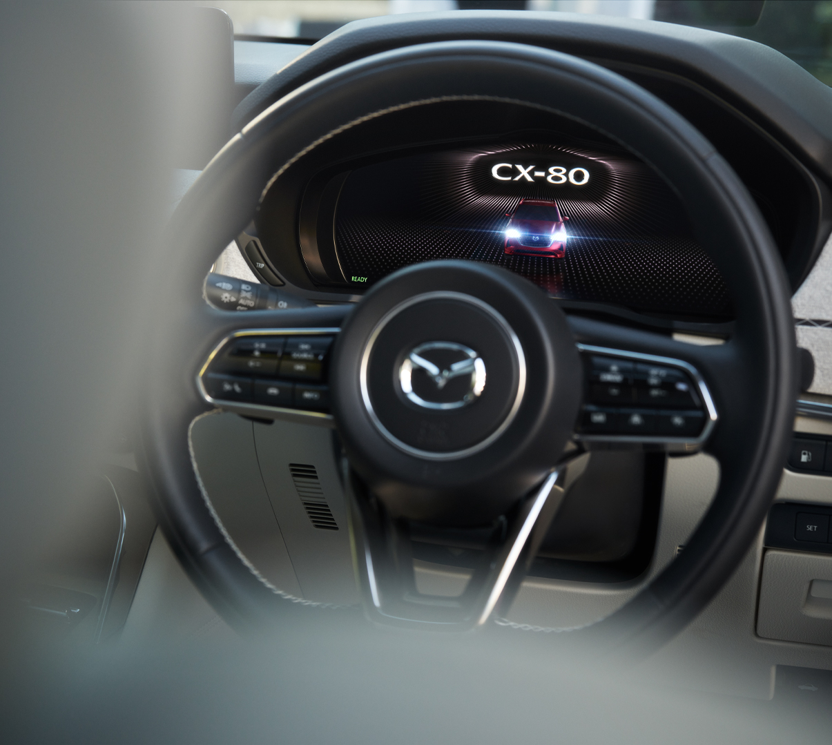 A close-up of the steering wheel of the Mazda CX-80 and its logo.