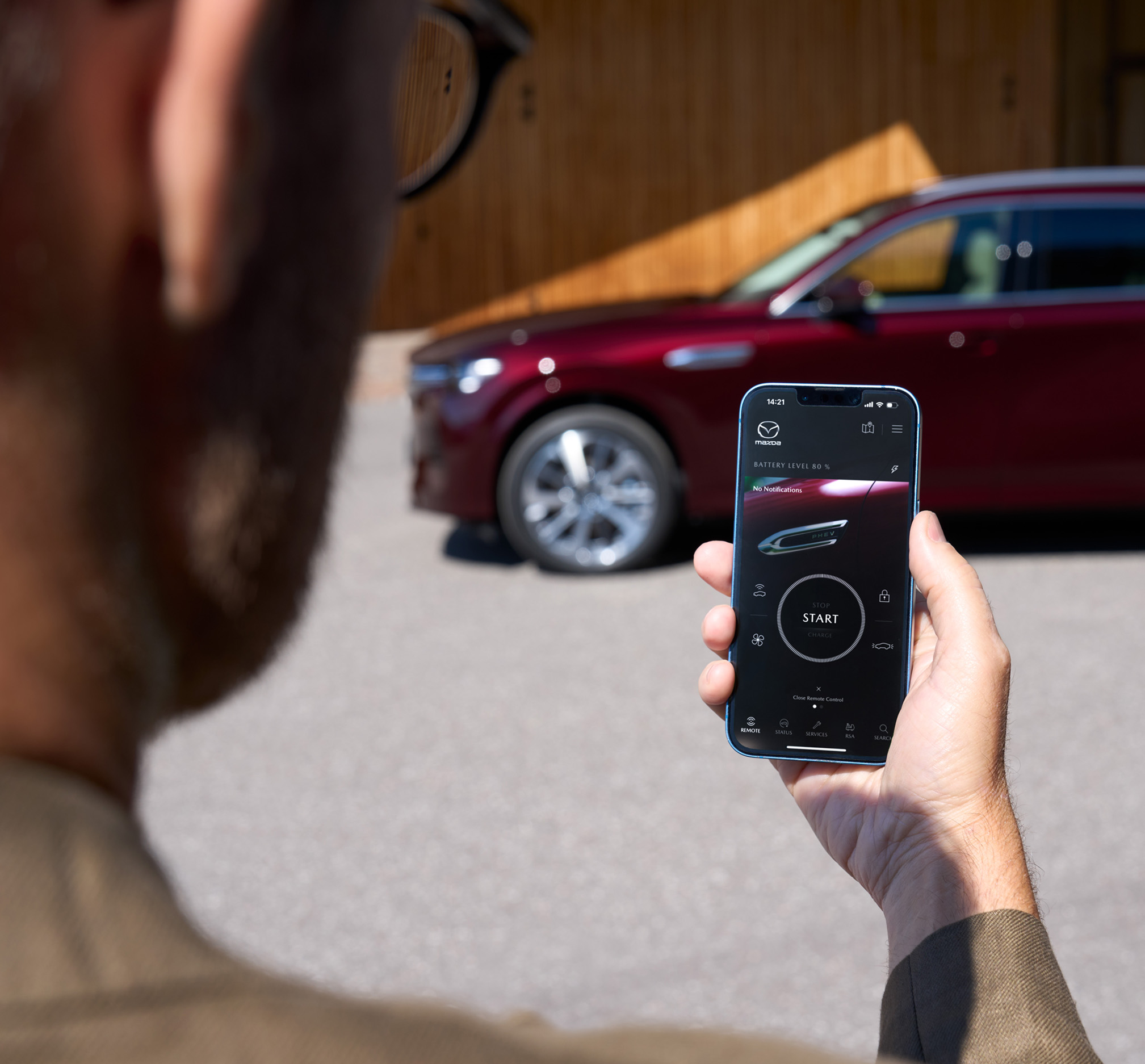 A man starting the charging process of his Mazda CX-80 using his smartphone and the myMazda App.