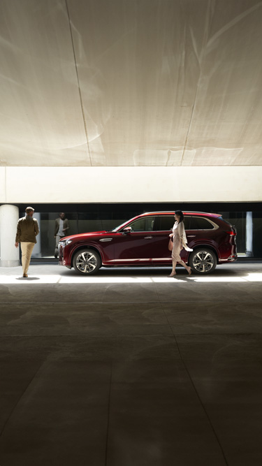 The Mazda CX-80 SUV parked in a garage and three people walking next to it.