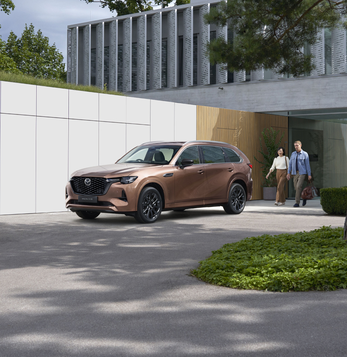 The Mazda CX-80 parked in front of a building with a couple walking to it.