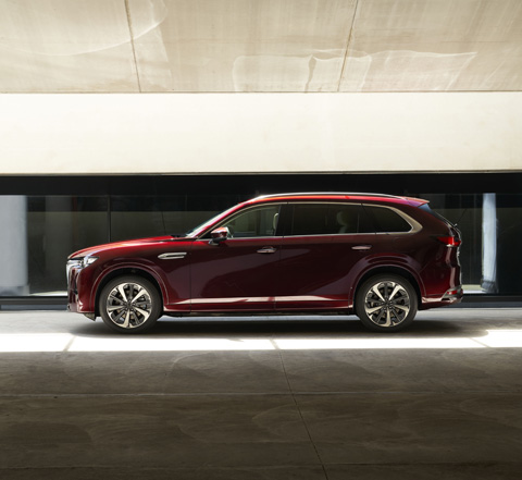 Vue latérale d'un SUV Mazda CX-80 rouge garé dans un immeuble.