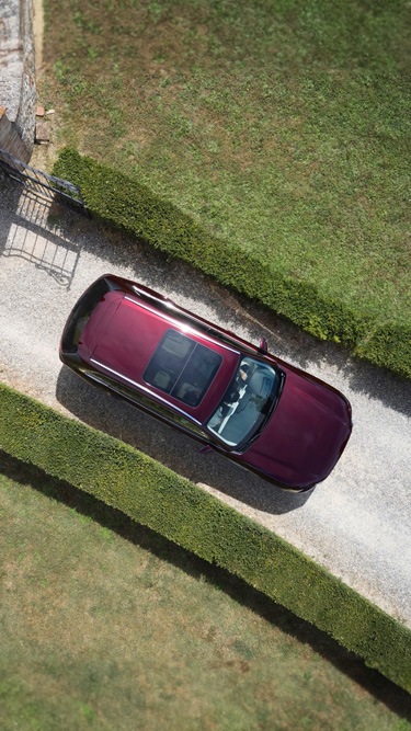 Vue de dessus d’un SUV Mazda CX-80 stationné dans une rue entre deux murs végétaux.