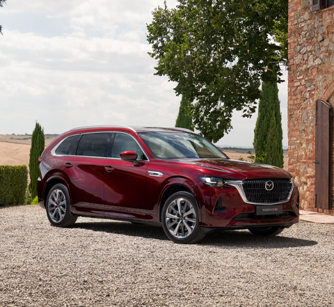 Zijkant van de Mazda CX-80, geparkeerd voor een huis met een glazen muur.