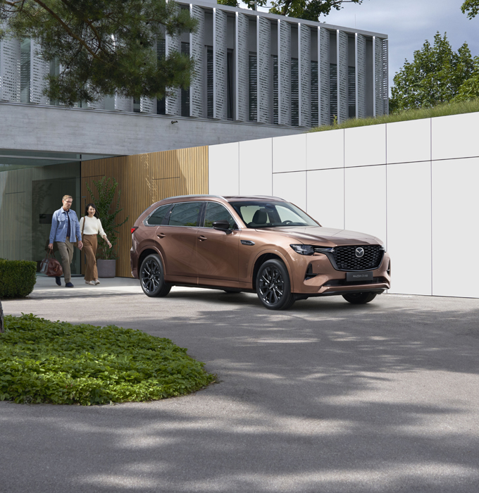 Mazda CX-80 estacionado em frente a um edifício com um casal a dirigir-se a ele.