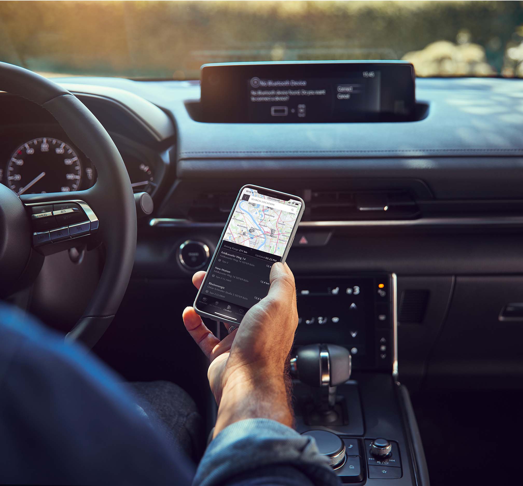 Ein Mann hält ein Smartphone mit der mobilen MyMazda-App in einem Mazda MX-30.