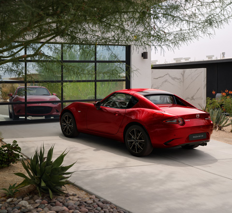 Ein roter Mazda MX-5
 RF, der vor einer verspiegelten Wand parkt.