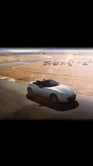 Το Mazda MX-5
 κινείται σε έναν ερημικό δρόμο με στροφές με την κουκούλα κατεβασμένη.