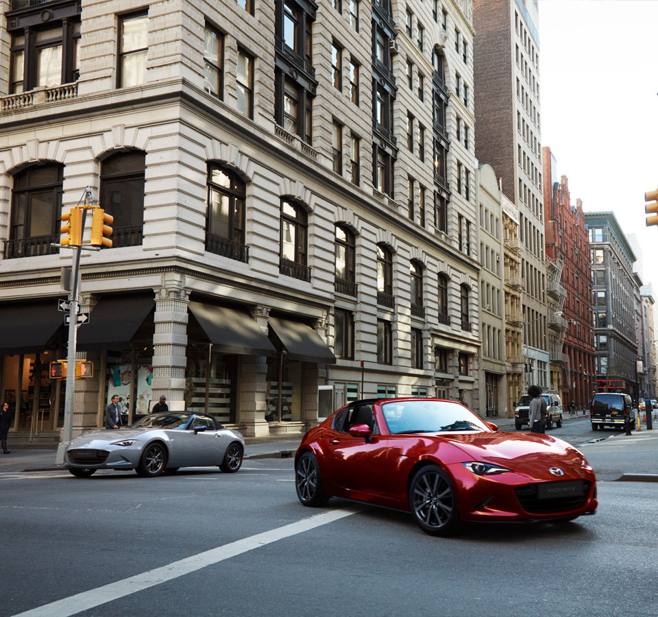 The Mazda MX 5 RF driving in front of the Mazda MX-5 Roadster in the city.