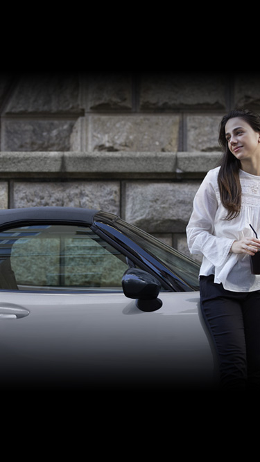 A woman leaning on the side of the Mazda MX-5 Roadster.