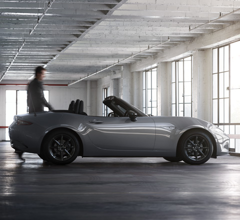 A man next to the Mazda MX-5
 Roadster inside an industrial space.