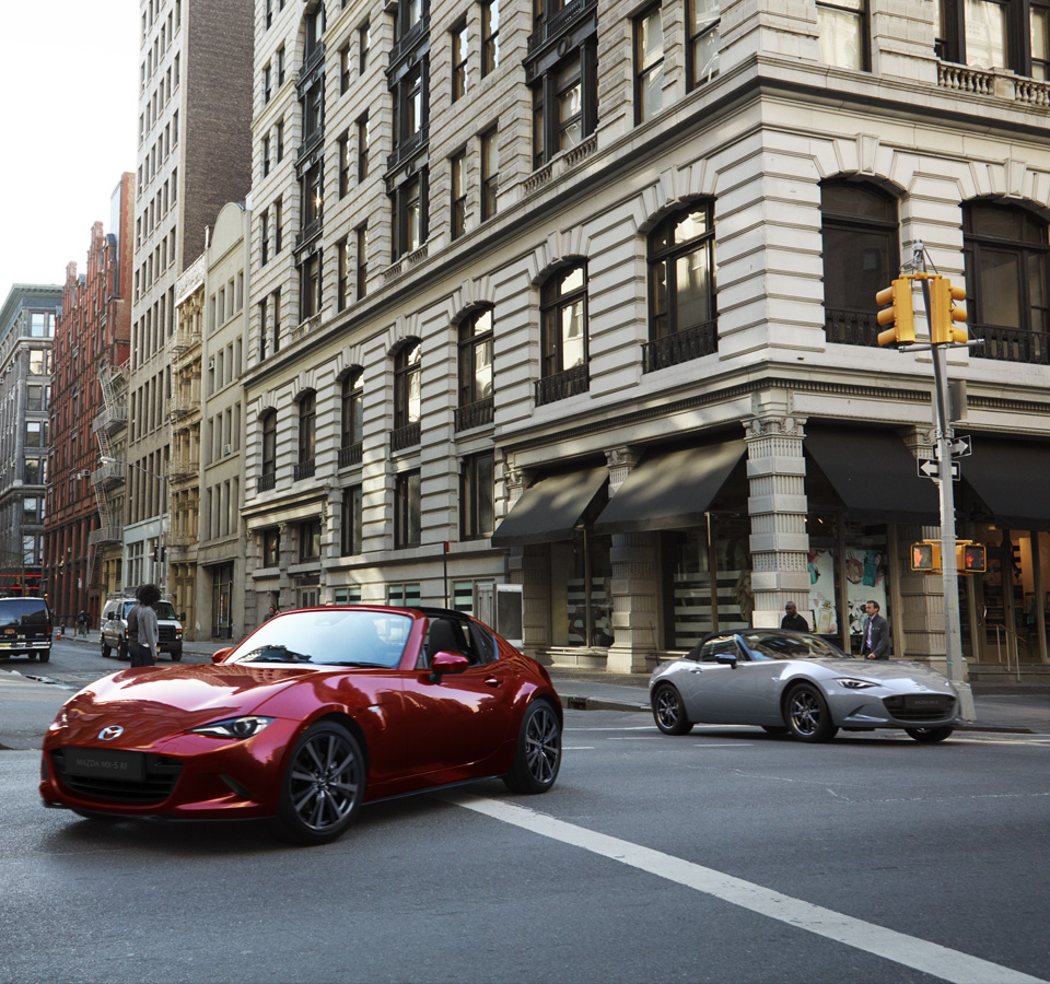 The Mazda MX 5 RF driving in front of the Mazda MX-5
 Roadster in the city.