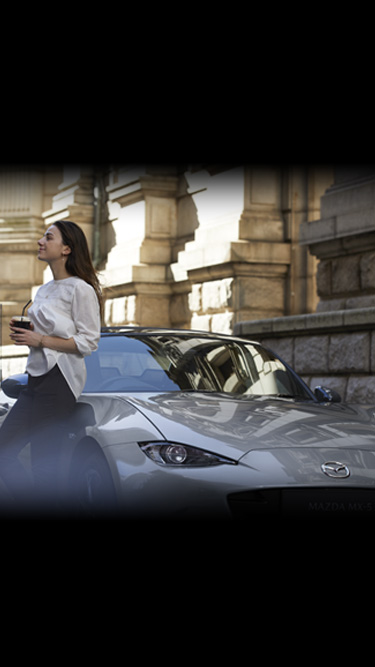 A woman leaning on the side of the Mazda MX-5
 holding a drink.