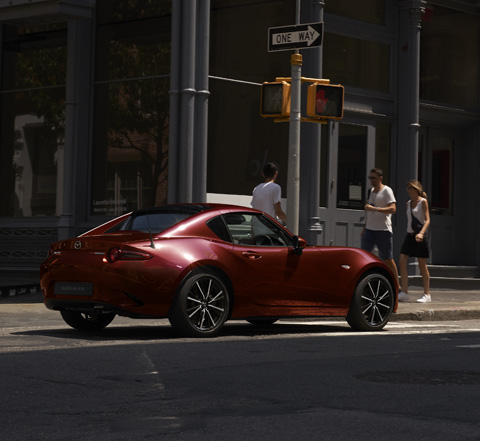 The Mazda MX 5 RF driving on the street in a city.