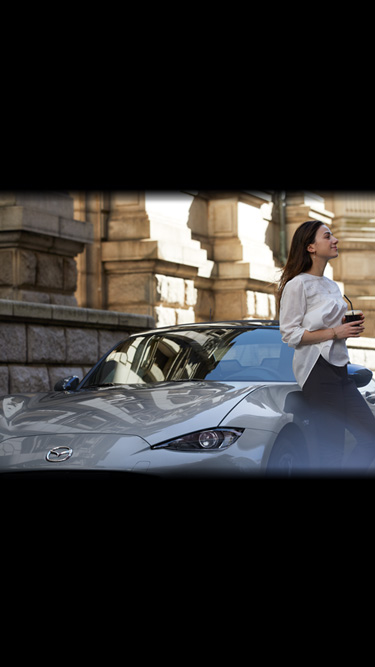 A woman leaning on the side of the Mazda MX-5 holding a drink.