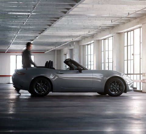 Un homme debout à côté d'une Mazda MX-5 Roadster dans un espace industriel.