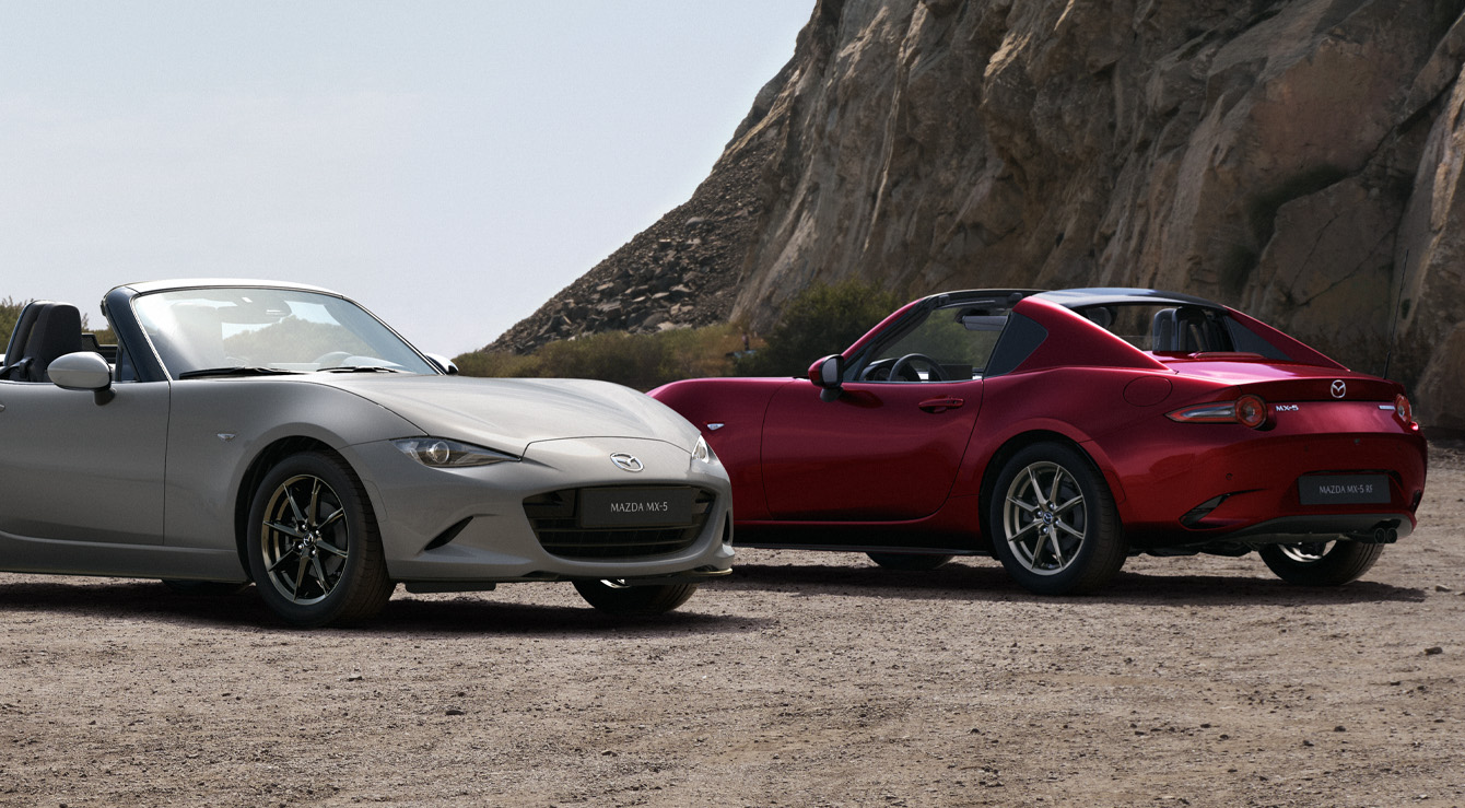 Mazda MX-5 Roadster og Mazda MX-5 RF parkeret ved siden af hinanden på stranden.