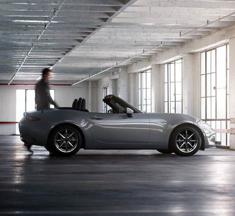 En mand ved siden af en Mazda MX-5 Roadster i et industrielt rum.