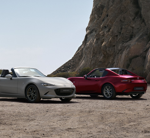 Mazda MX-5 Roadster og Mazda MX-5 RF parkeret ved siden af hinanden på stranden.