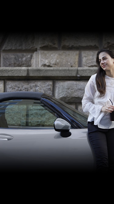 Žena naslonjena na bočnu stranu modela Mazda MX-5 Roadster.